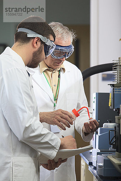 Ein Professor arbeitet mit einem Ingenieurstudenten zusammen  der Ethanol in ein Probentablett in einem Labor einfüllt.