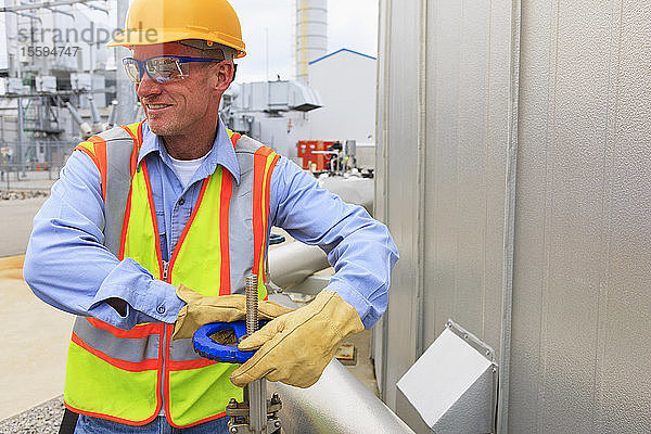 Ingenieur in einem Elektrizitätswerk  der einen Schieber an einem Rohr zum Wasserspeichertank dreht