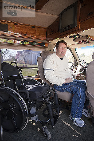 Mann mit Querschnittslähmung steigt aus seinem Rollstuhl in den Fahrersitz eines behindertengerechten Transporters