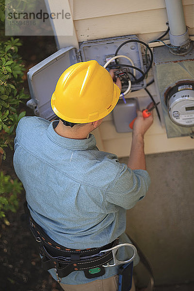 Elektriker bei Arbeiten an einem Kabel im Anschlusskasten eines Hauses