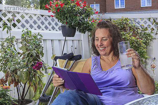 Frau mit Spina Bifida arbeitet auf der Terrasse an einem Tablet und genießt ein Getränk