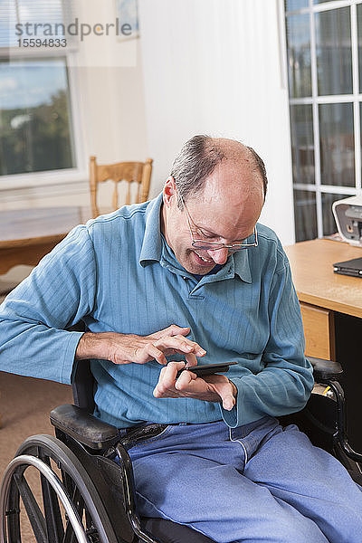 Mann mit Friedreich-Ataxie im Rollstuhl benutzt ein Smartphone mit deformierten Händen