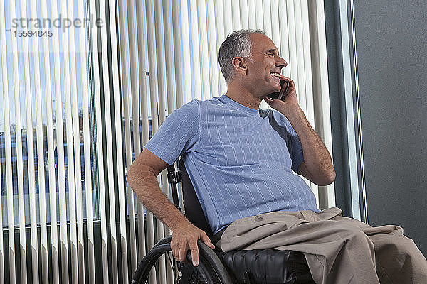 Mann mit Querschnittslähmung im Rollstuhl telefoniert in einem Büro