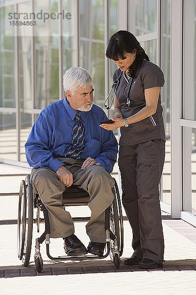 Mann mit Muskeldystrophie und Diabetes in seinem Rollstuhl im Gespräch mit einer Krankenschwester über ein Smartphone