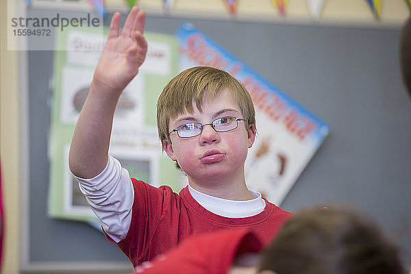Junge mit Down-Syndrom hebt die Hand in einem Klassenzimmer