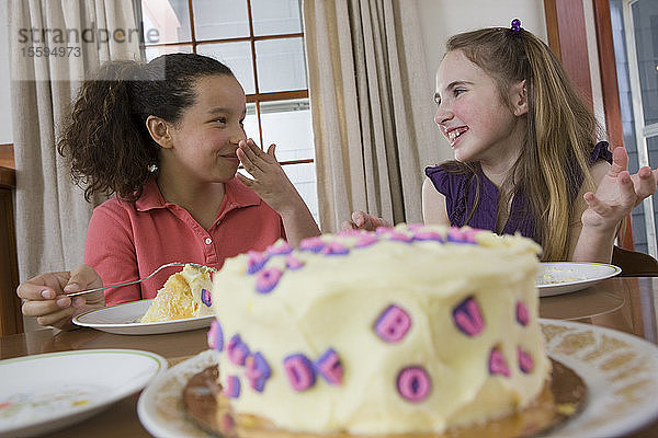 Zwei Mädchen essen Geburtstagskuchen und lächeln