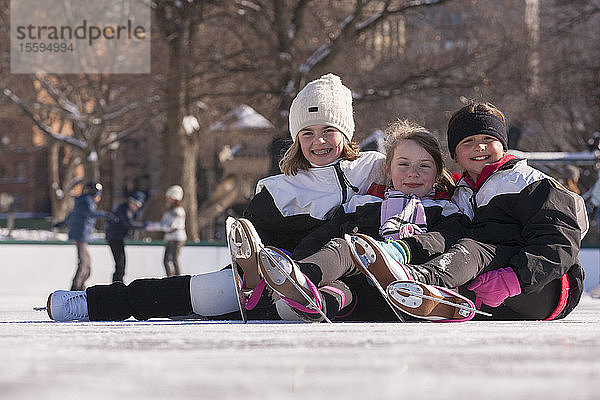 Mädchen sitzen auf dem Eis in einer Eislaufhalle