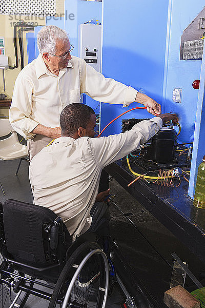 Ausbilder bespricht das Aufladen von Klimaanlagen mit einem Schüler im Rollstuhl im HVAC-Klassenzimmer