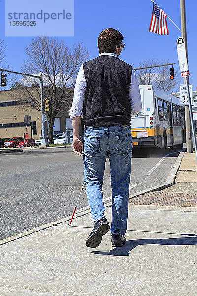 Junger blinder Mann mit Blindenstock auf dem Weg zu einer Bushaltestelle