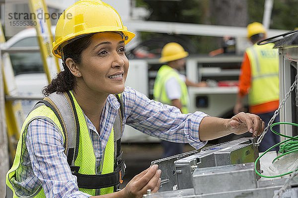 Hispanische Mitarbeiterin eines Versorgungsunternehmens bei der Arbeit mit Leitungsverstärkern auf der Baustelle