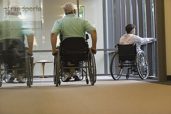 Älterer Mann mit Muskeldystrophie und eine junge Frau sitzen im Rollstuhl in einer Bibliothek