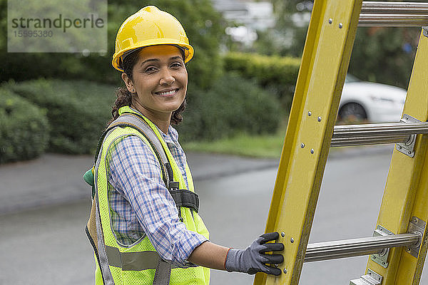 Porträt einer glücklichen hispanischen Elektrikerin bei der Arbeit an einer Stromleitung vor Ort