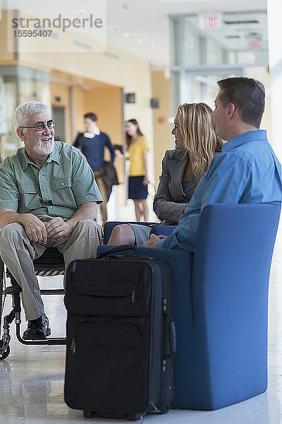 Fluggäste  die sich in einer Flughafenlounge unterhalten  einer davon mit Muskeldystrophie