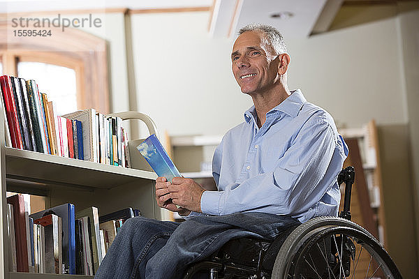 Mann im Rollstuhl mit einer Rückenmarksverletzung wählt Bücher aus einem Regal in einer Bibliothek aus