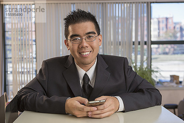 Porträt eines glücklichen asiatischen Mannes mit Autismus  der sein Telefon in einem Büro benutzt