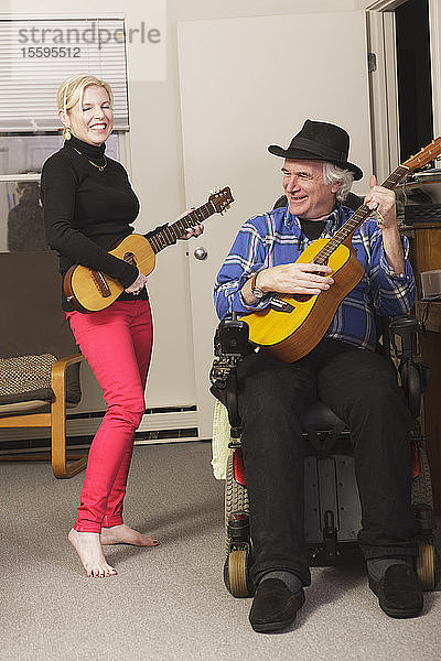 Musiker mit Multipler Sklerose in einem motorisierten Rollstuhl mit seiner Gitarre und seinem Partner