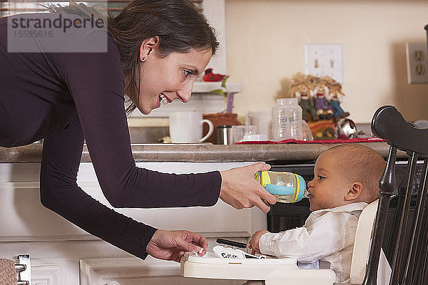 Mutter füttert ihren Sohn  der aus einer Schnabeltasse trinkt