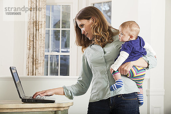 Frau arbeitet zu Hause am Computer und hält ihr Baby