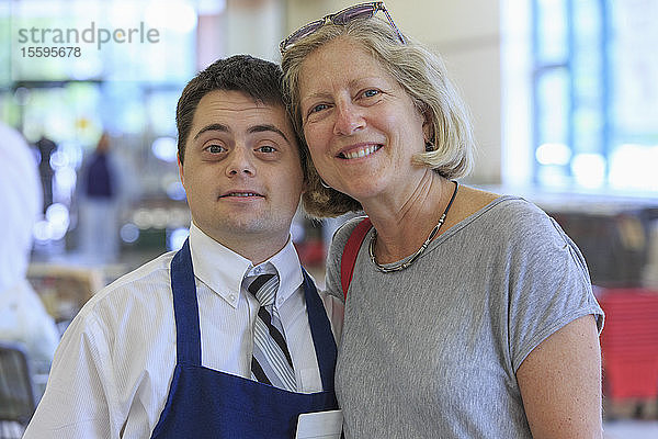 Porträt eines Mannes mit Down-Syndrom  der in einem Lebensmittelladen arbeitet und einen Kunden begrüßt
