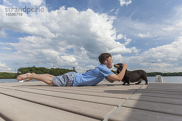 Junger Mann mit Down-Syndrom spielt mit einem Hund auf einem Steg