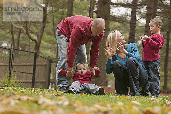 Frau  die das Wort Familie in amerikanischer Zeichensprache gebärdet  während sie mit ihrer Familie in einem Park spielt