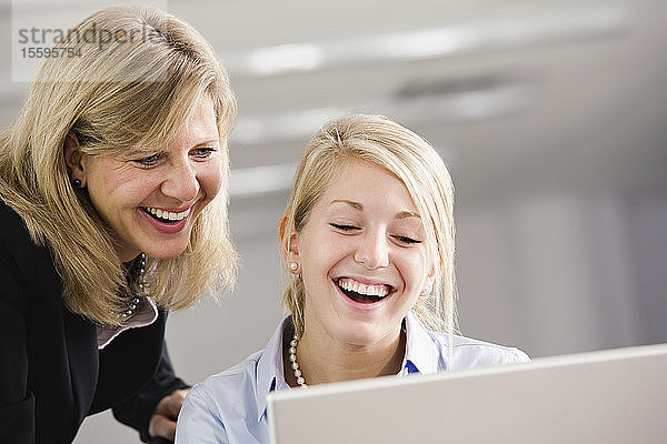 Zwei Geschäftsfrauen schauen auf einen Laptop und lächeln.