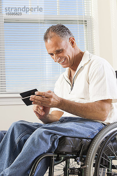 Mann mit Rückenmarksverletzung im Rollstuhl benutzt ein Smartphone