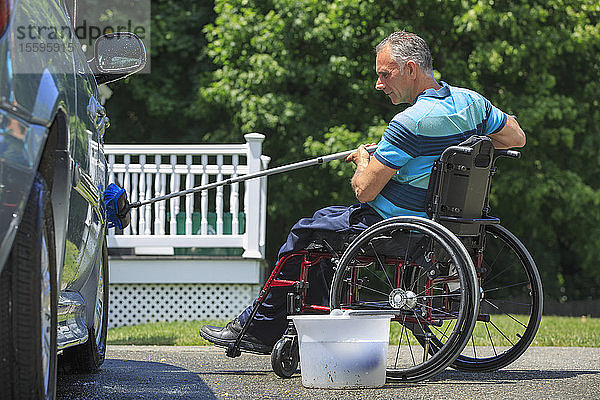 Ein Mann mit einer Rückenmarksverletzung im Rollstuhl wäscht sein zugängliches Auto