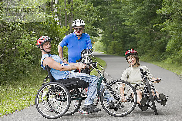 Porträt eines jungen Mannes mit einer Rückenmarksverletzung und seiner Freunde auf adaptiven Fahrrädern
