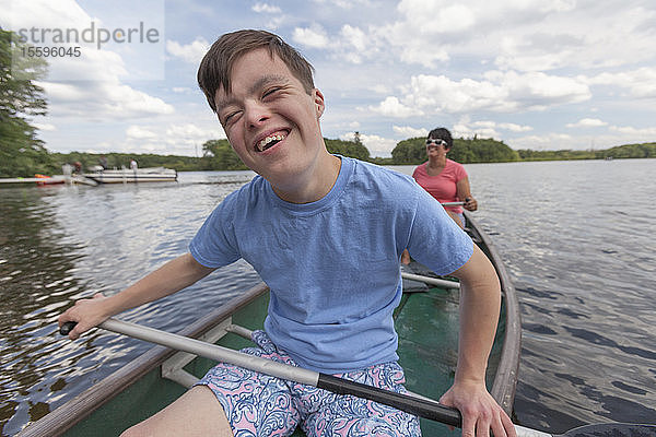 Glücklicher junger Mann mit Down-Syndrom rudert mit seinem Freund in einem Kanu auf einem See