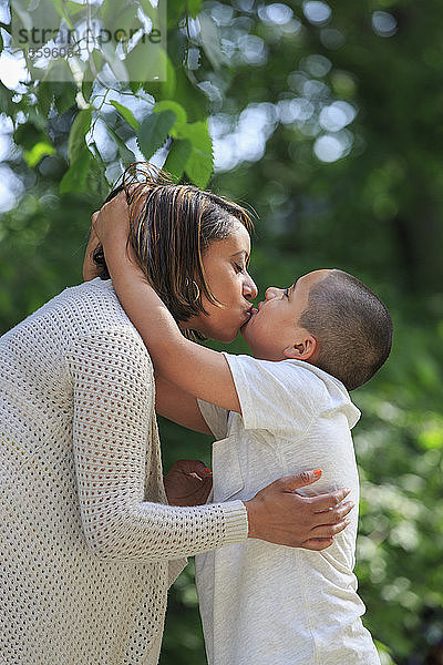 Hispanischer Junge mit Autismus küsst seine Mutter im Park