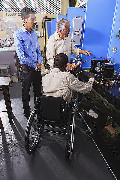 Ausbilder bespricht das Aufladen von Klimaanlagen mit Schülern im HLK-Klassenzimmer  ein Schüler sitzt im Rollstuhl