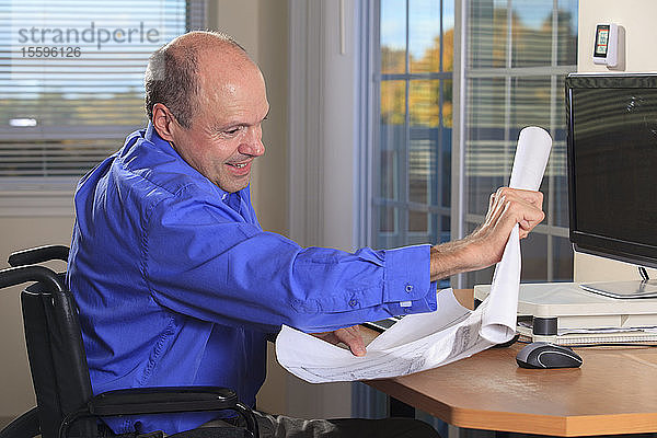 Mann mit Friedreich-Ataxie und deformierten Händen als Elektronikkonstrukteur an seinem Arbeitsplatz bei der Überprüfung von Plänen