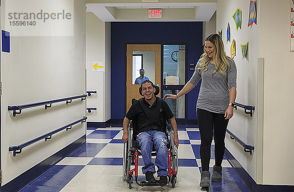 Junge mit spastischer Tetraplegie und Zerebralparese geht mit Lehrer den Schulflur entlang