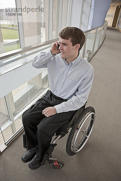 Geschäftsmann mit Querschnittslähmung im Rollstuhl  der mit einem Mobiltelefon spricht