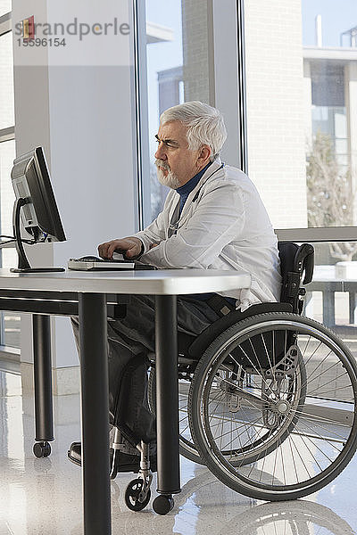 Arzt mit Muskeldystrophie im Rollstuhl studiert Informationen auf seinem Computer