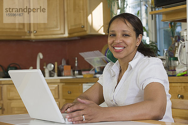 Hispanische Geschäftsfrau  die in der Küche an einem Laptop arbeitet