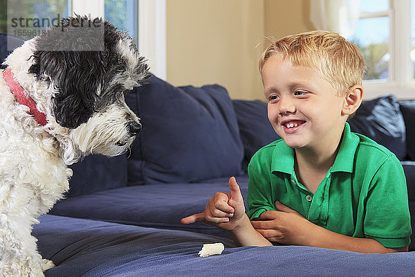 Junge mit Hörbehinderung gebärdet stay in amerikanischer Gebärdensprache auf ihrer Couch