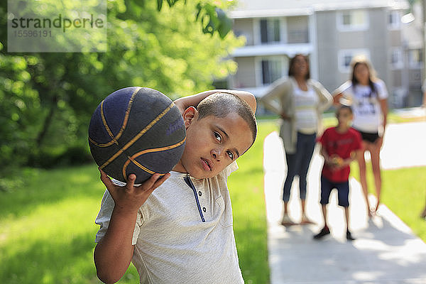 Hispanischer Junge mit Autismus  der mit seiner Familie draußen mit einem Ball spielt