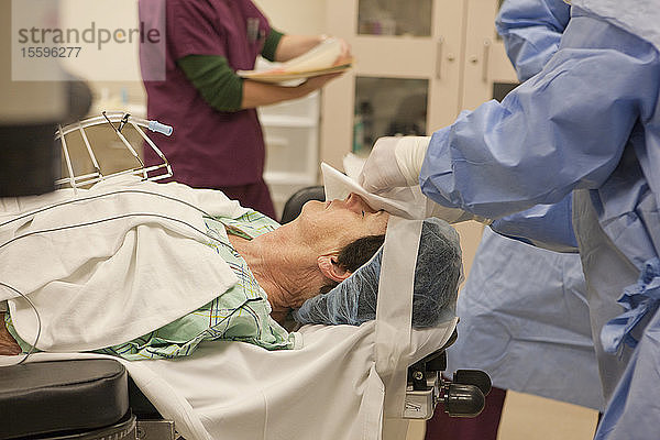 Chirurgische Technologin  die einem Patienten ein steriles Tuch für eine Kataraktoperation ins Auge legt
