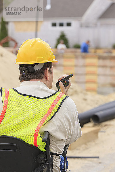 Bauleiter mit Querschnittslähmung am Walkie Talkie mit Fundament und Rohren im Hintergrund