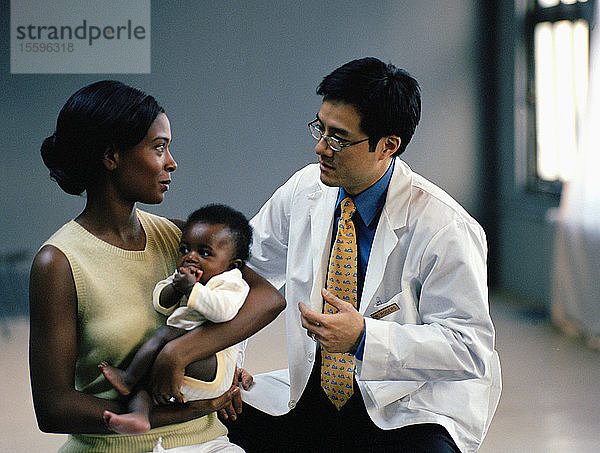 Junge Frau  die ihr kleines Baby hält  während ihr männlicher Arzt dabei ist