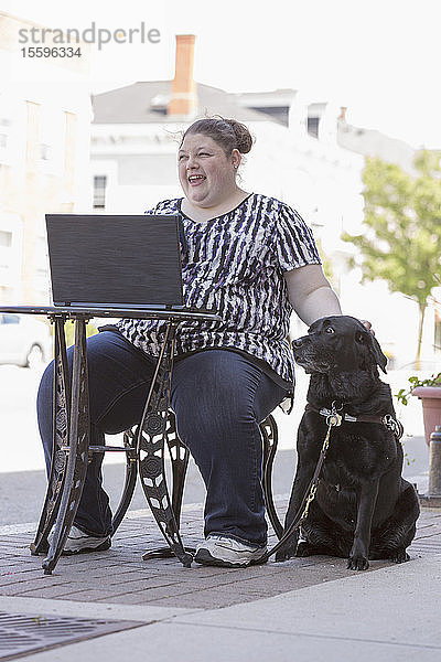 Frau mit Sehbehinderung sitzt mit ihrem Computer und ihrem Diensthund in einem CafÃƒÂ©