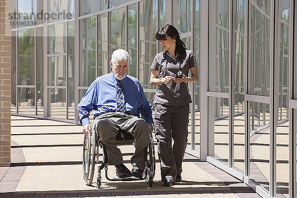 Mann mit Muskeldystrophie und Diabetes in seinem Rollstuhl geht mit einer Krankenschwester  die ein Smartphone benutzt