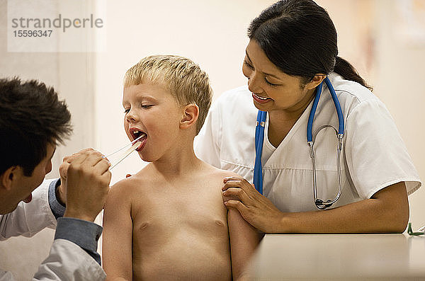Ein Arzt untersucht den Rachen eines Jungen mit einem Zungenspatel.