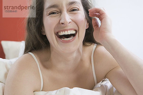Porträt einer mittleren erwachsenen Frau  die auf dem Bett liegt und lacht