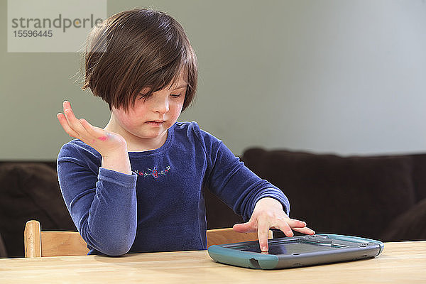 Kleines Mädchen mit Down-Syndrom spielt ein elektronisches Lernspiel