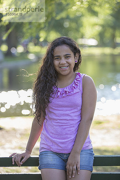 Porträt eines glücklichen hispanischen Teenager-Mädchens mit Zahnspange  das im Park sitzt