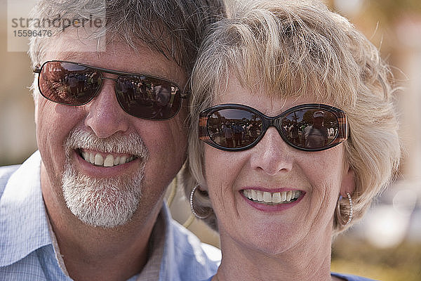 Nahaufnahme eines lächelnden Paares mit Spiegelung eines Shuffleboard-Spiels in einer Sonnenbrille