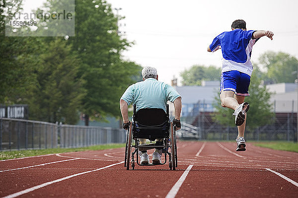 Rückansicht eines jungen Mannes  der mit einem an Muskeldystrophie leidenden Mann im Rollstuhl um die Wette fährt